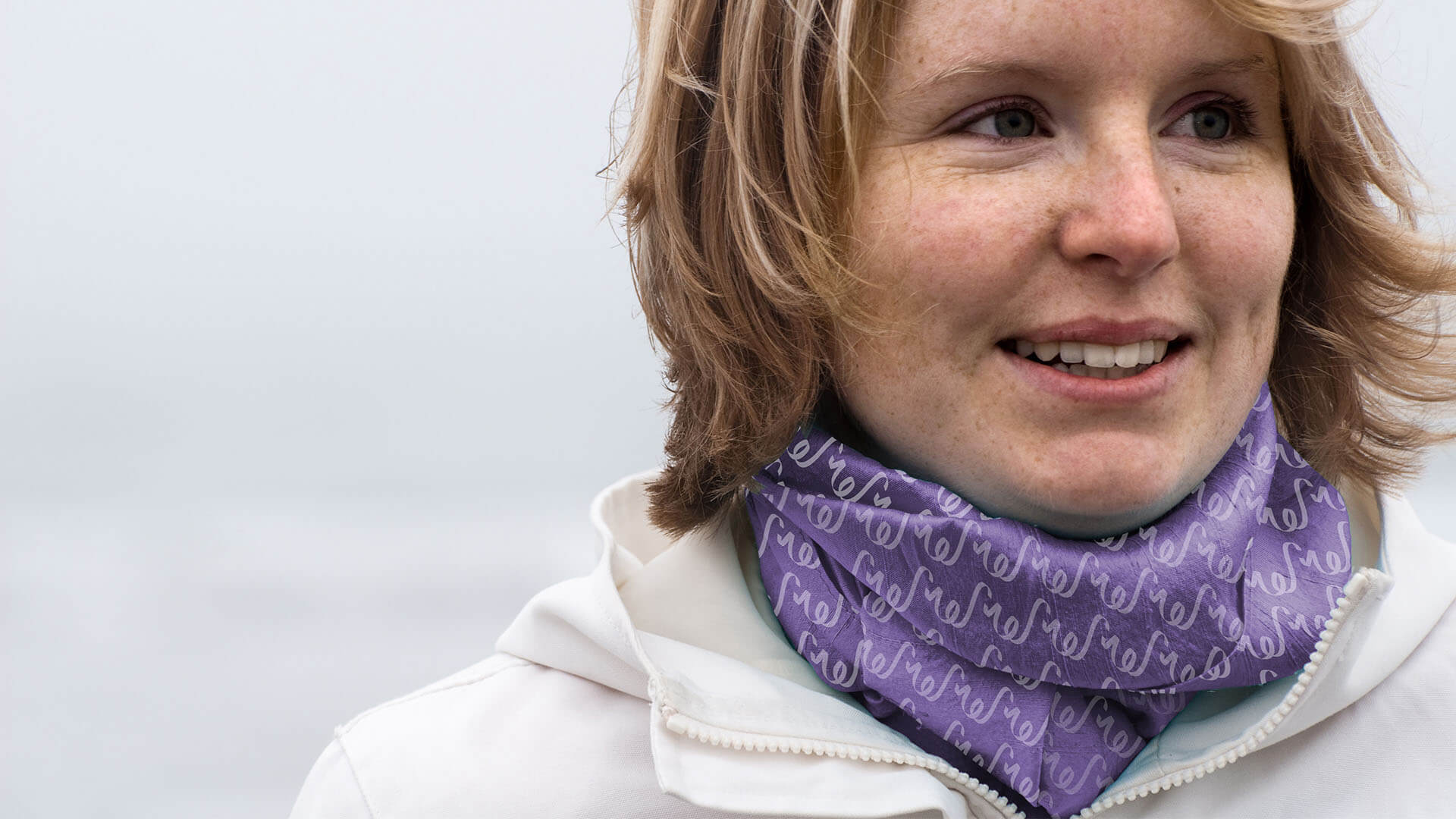 A woman wearing a scarf with the brand pattern in white over a purple background